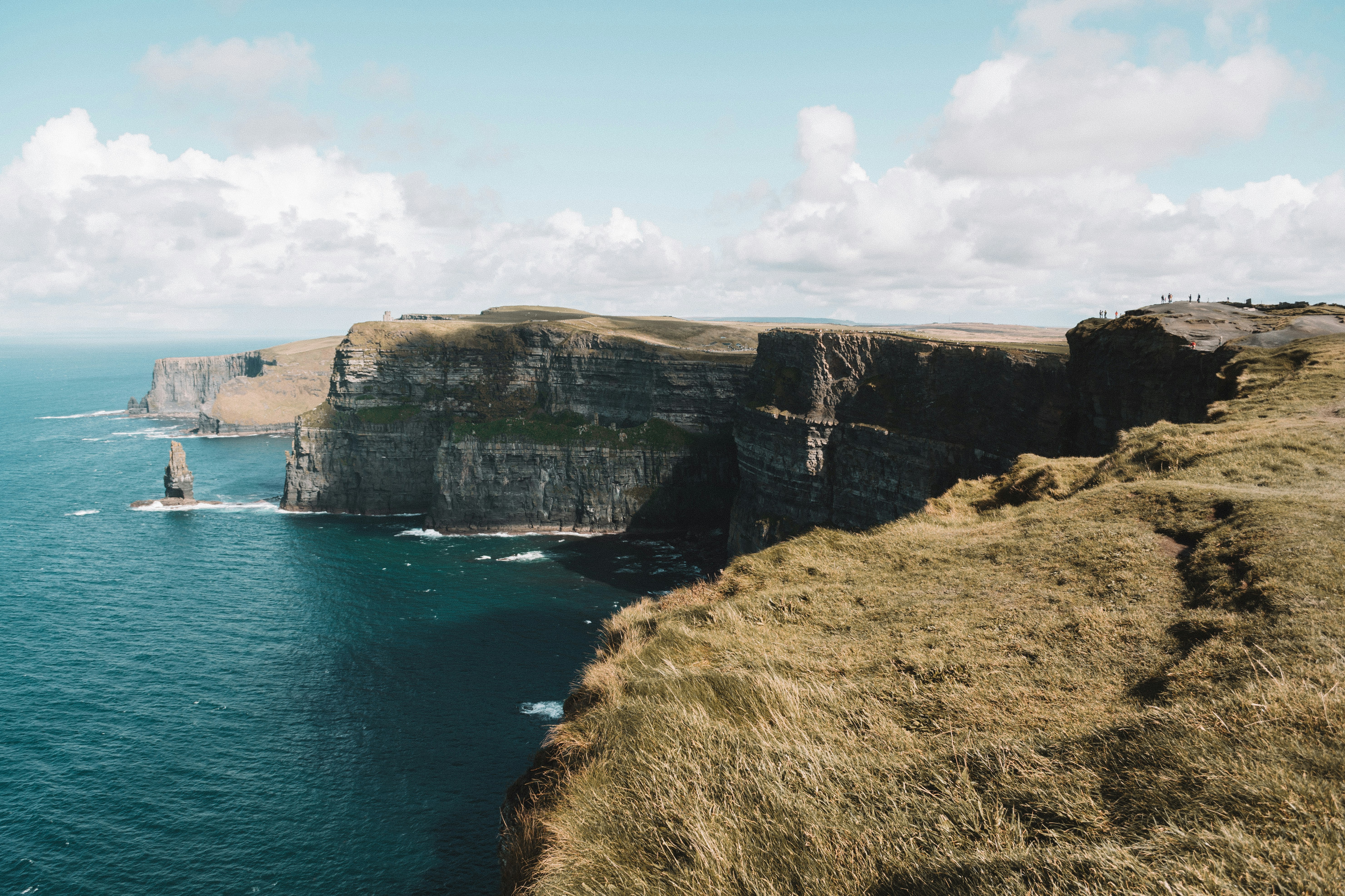 beach cliff viewing blue sea under white and blue skies during daytime